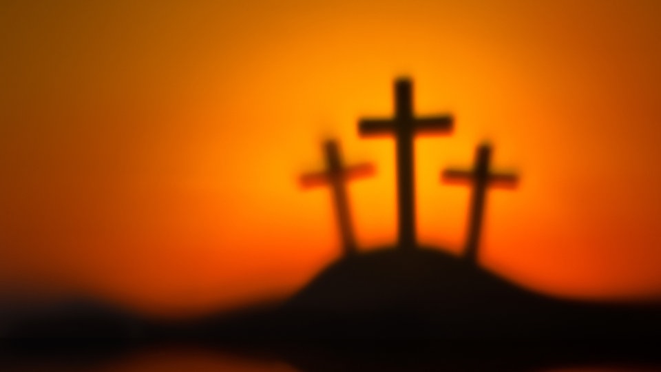 Drei schwarze Kreuze auf einem Hügel, der Hintergrund orange