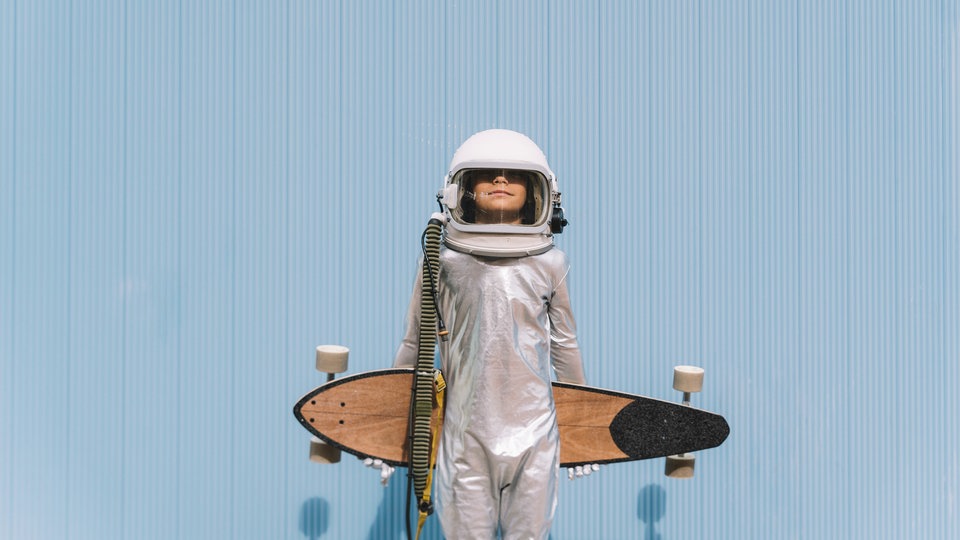 Ein Junge in Astronauten-Kostüm hält ein Longboard in den Armen
