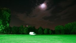 Ein Park bei Nacht, der Mond scheint durch die Wolgen, auf der Parkwiese steht ein Van