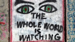 Ein Graffiti auf der Wand: zwei Augen mit der Unterschrift "the whole world is watching"
