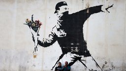Zwei Männer sitzen vor einem Graffiti von Banksy