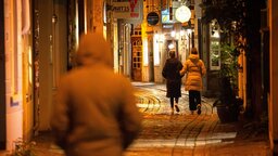 Passanten gehen am späten Abend in einer dunklen Gasse