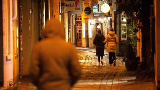 Passanten gehen am späten Abend in einer dunklen Gasse