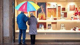 Zwei §ltere Personen stehen bei Regen vor einem Schaufenster eines Schmuckgesch §fts