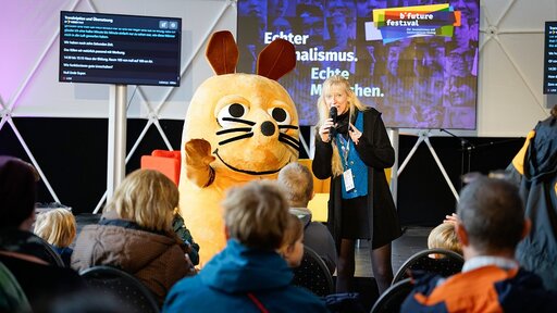 Die Maus und Reporterin Insa Backe (hier beim b*future festival 2025) werden auch dieses Jahr wieder vor Ort sein